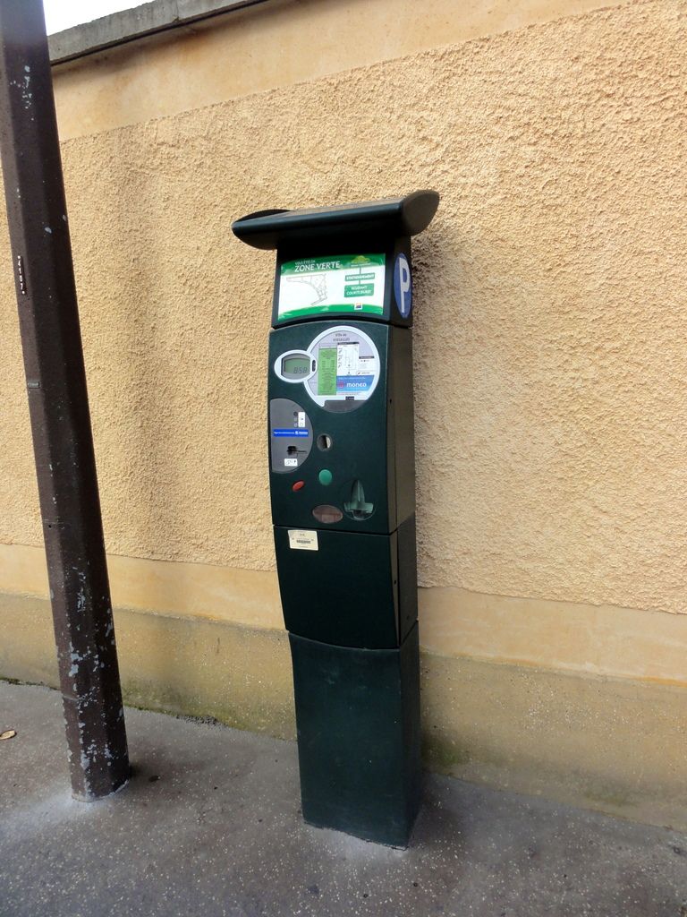 In the image there is an atm machine in front of the wall beside a pole.
